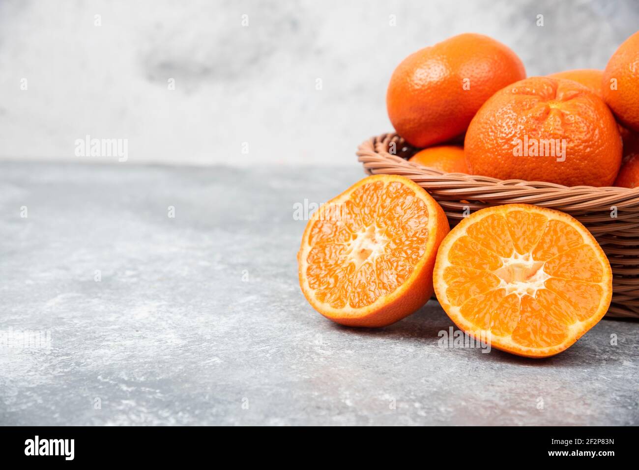 A wicker box full of juicy orange fruits on stone background Stock Photo