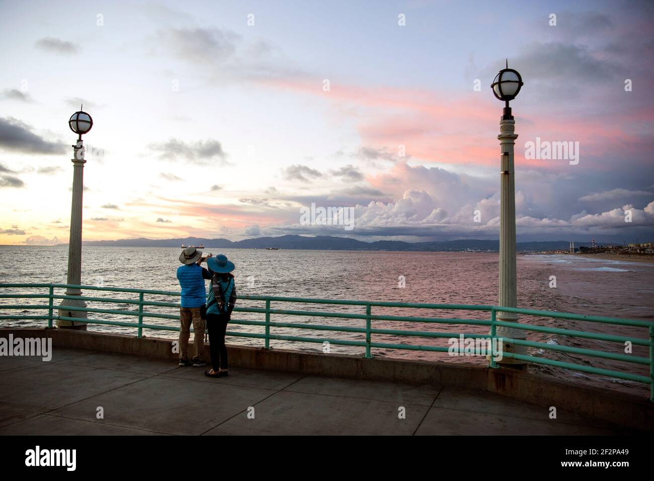 Couple taking photographs of dramatic sunset from the Manhattan Beach Pier in Los Angeles' South Bay area. Stock Photo