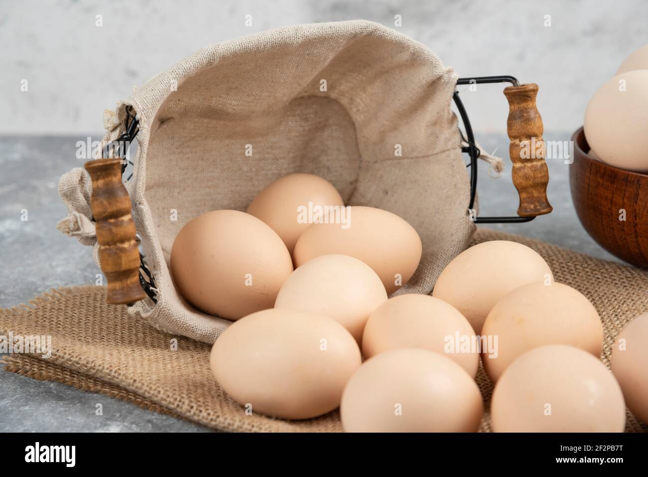 Basket and bowl full of organic fresh uncooked eggs on marble surface Stock Photo
