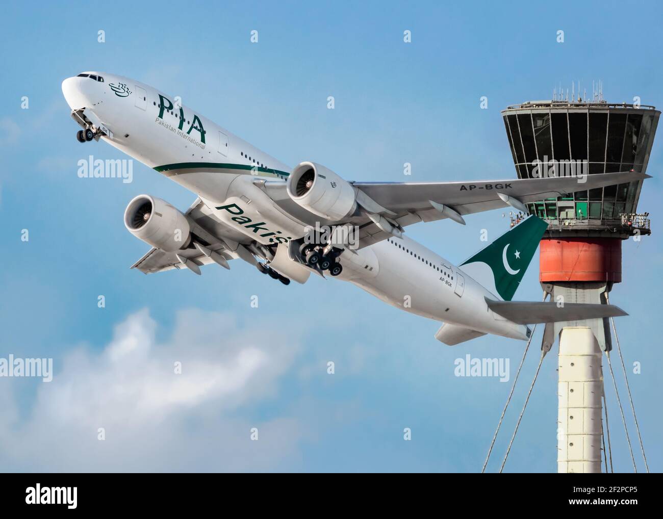 London, Heathrow Airport - April, 2019: Pakistan International Airline (PIA) taking off with retracting landing gear into a bright sky with the tower Stock Photo