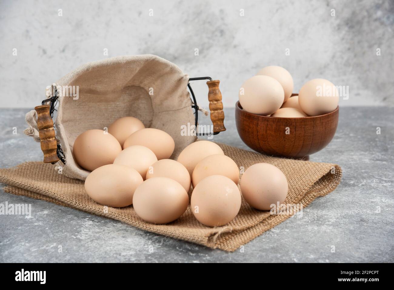 Basket and bowl full of organic fresh uncooked eggs on marble surface Stock Photo