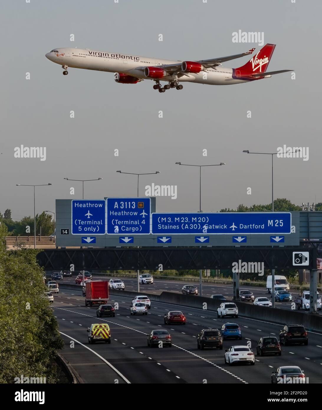 London Heathrow, UK, June 2019. Virgin Atlantic Airbus A340 flying over the busy M25 Motorway Gantry and road signs whilst fast moving road traffic fl Stock Photo
