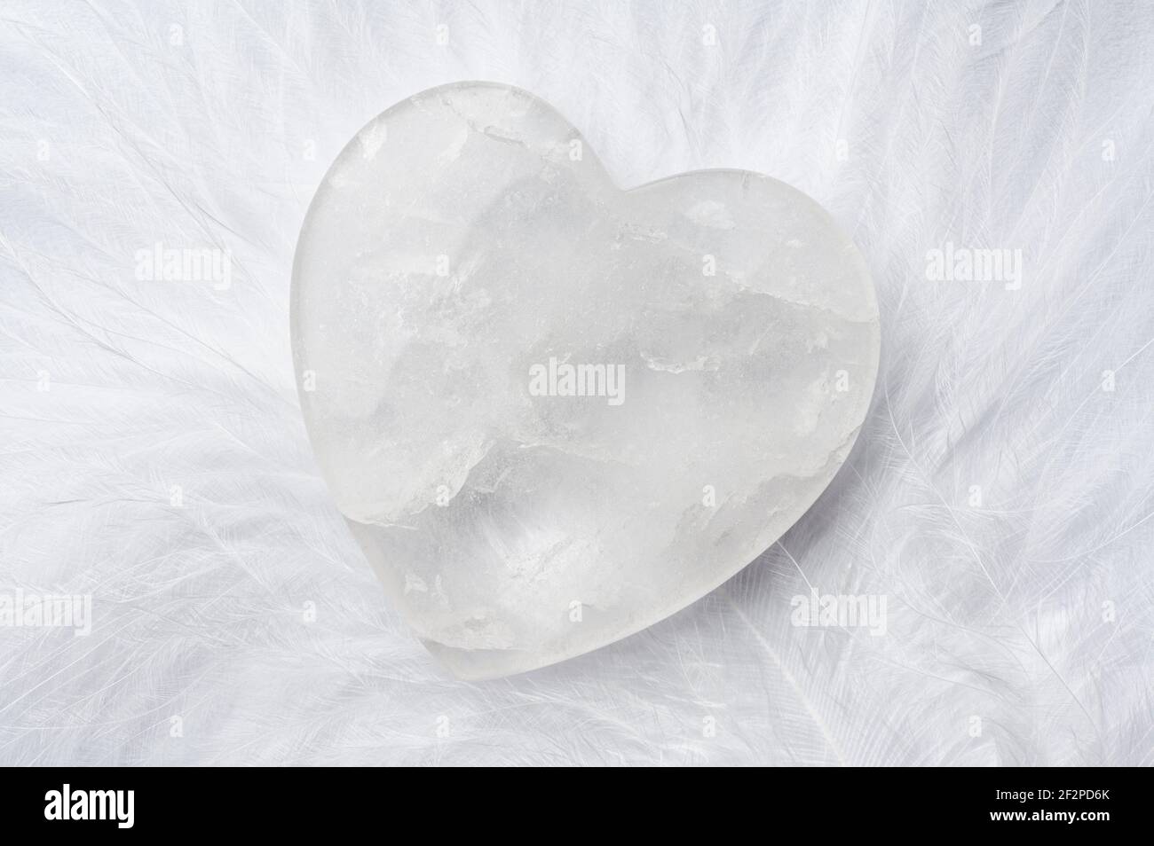 Rock crystal heart on white down feather, symbol of purity, innocence Stock Photo