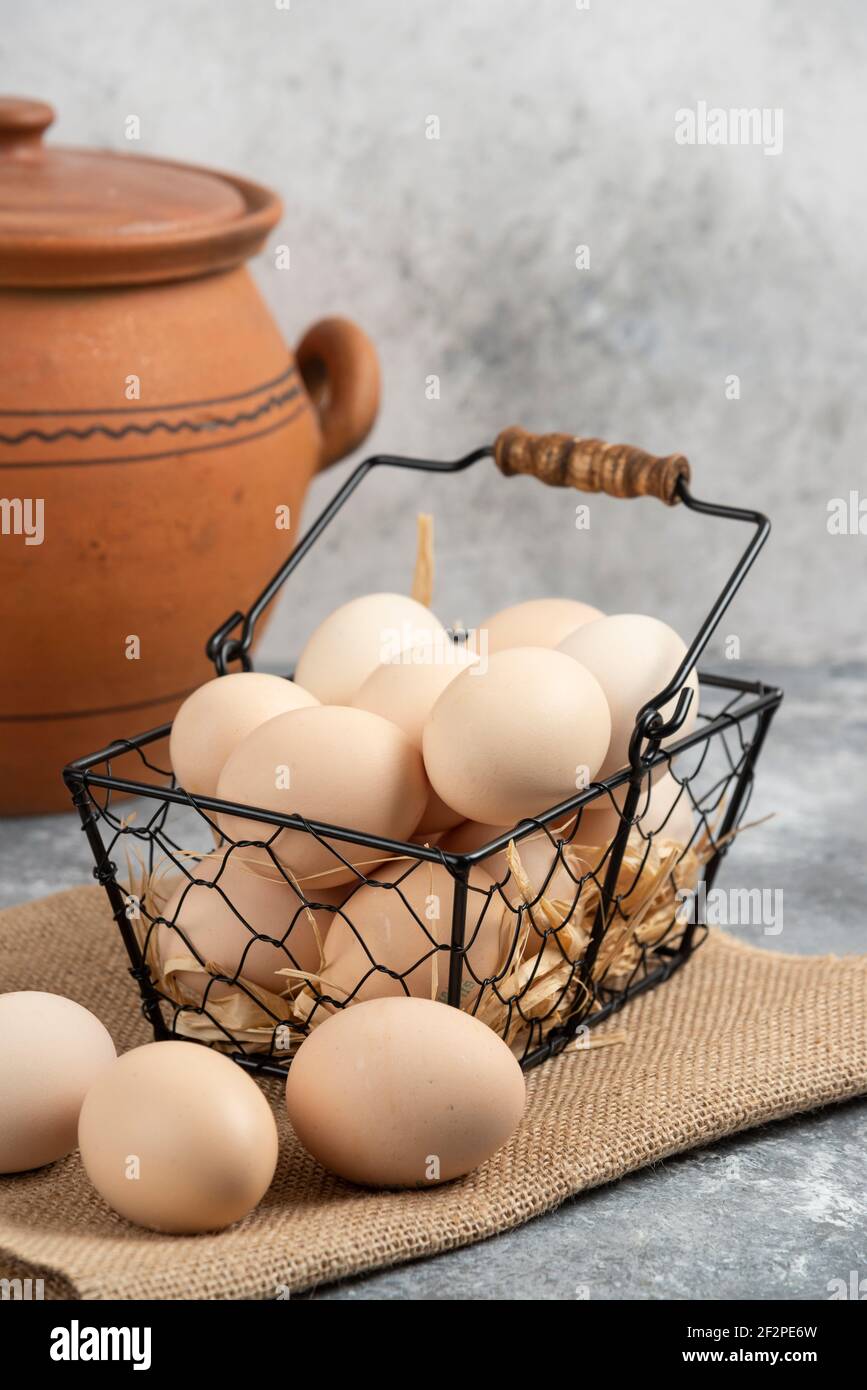Metal basket of raw chicken eggs and antique vase on marble surface Stock Photo
