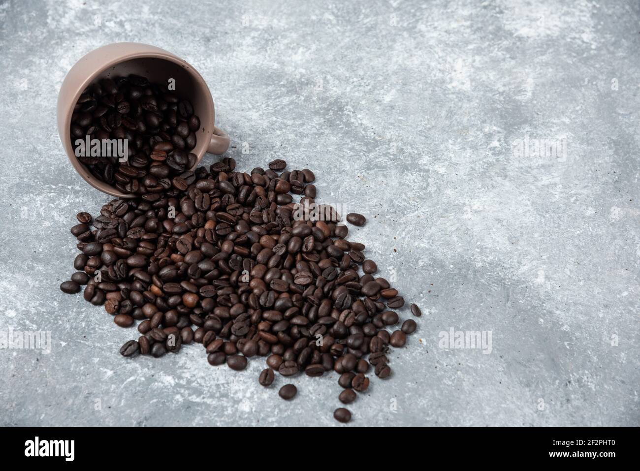Aromatic roasted coffee beans out of cup on marble surface Stock Photo
