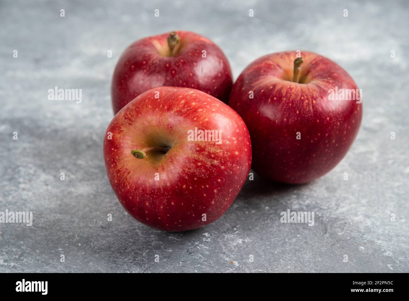 Three ripe red apples placed on marble surface Stock Photo