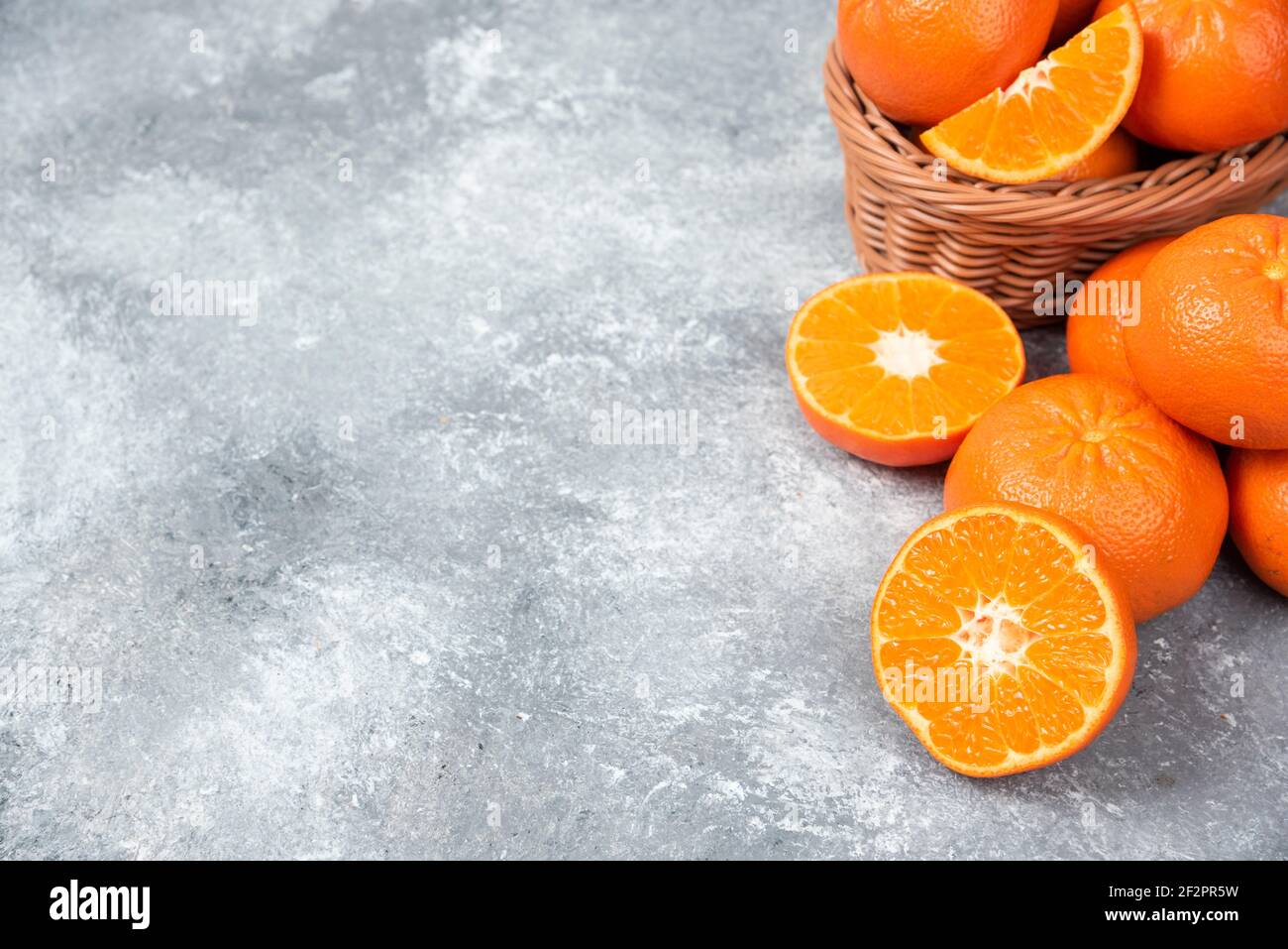 Whole and slice juicy fresh orange fruits in a wicker basket placed Stock Photo