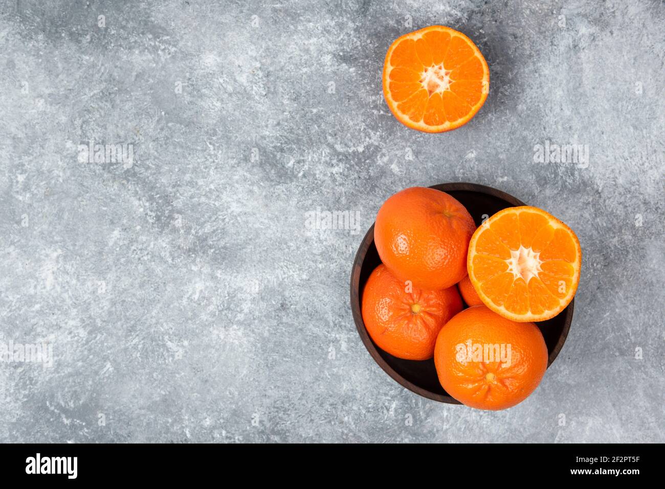 A wooden bowl full of juicy orange fruits on stone background Stock Photo