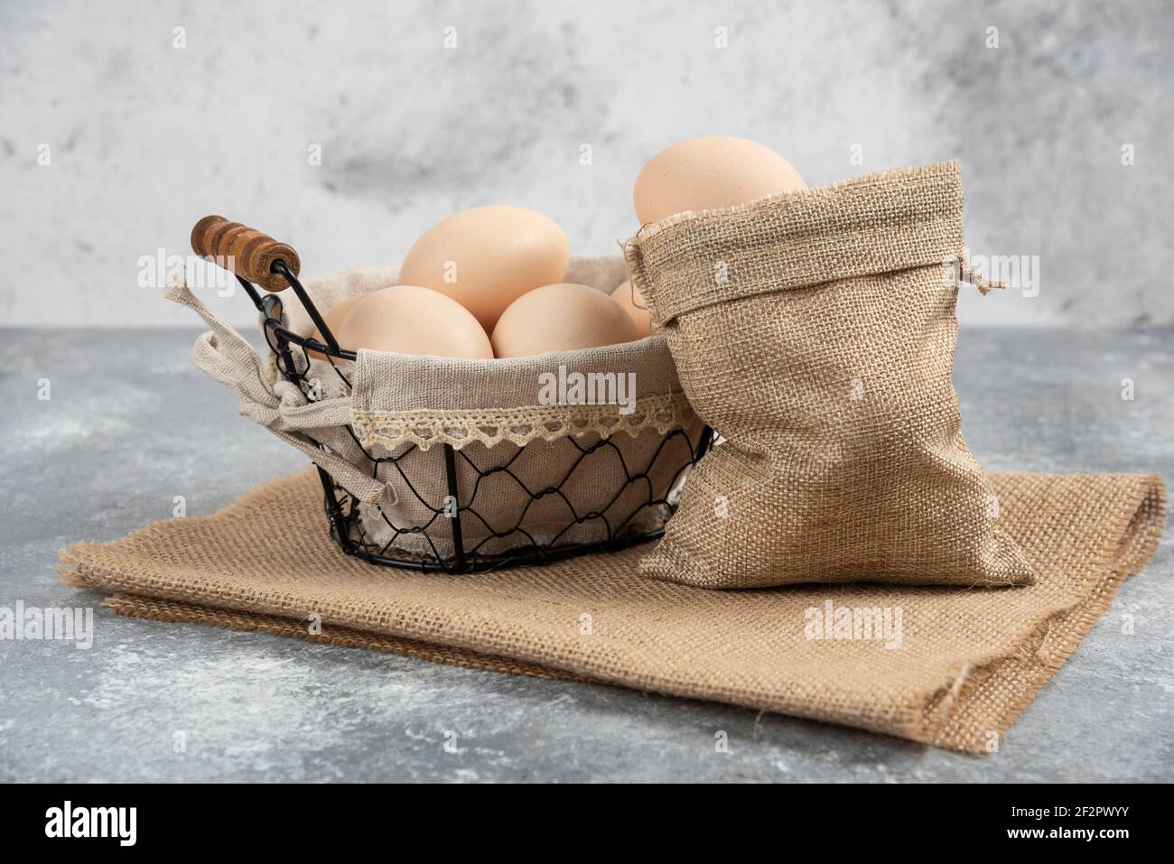 Basket and sackcloth of organic fresh uncooked eggs on marble surface Stock Photo