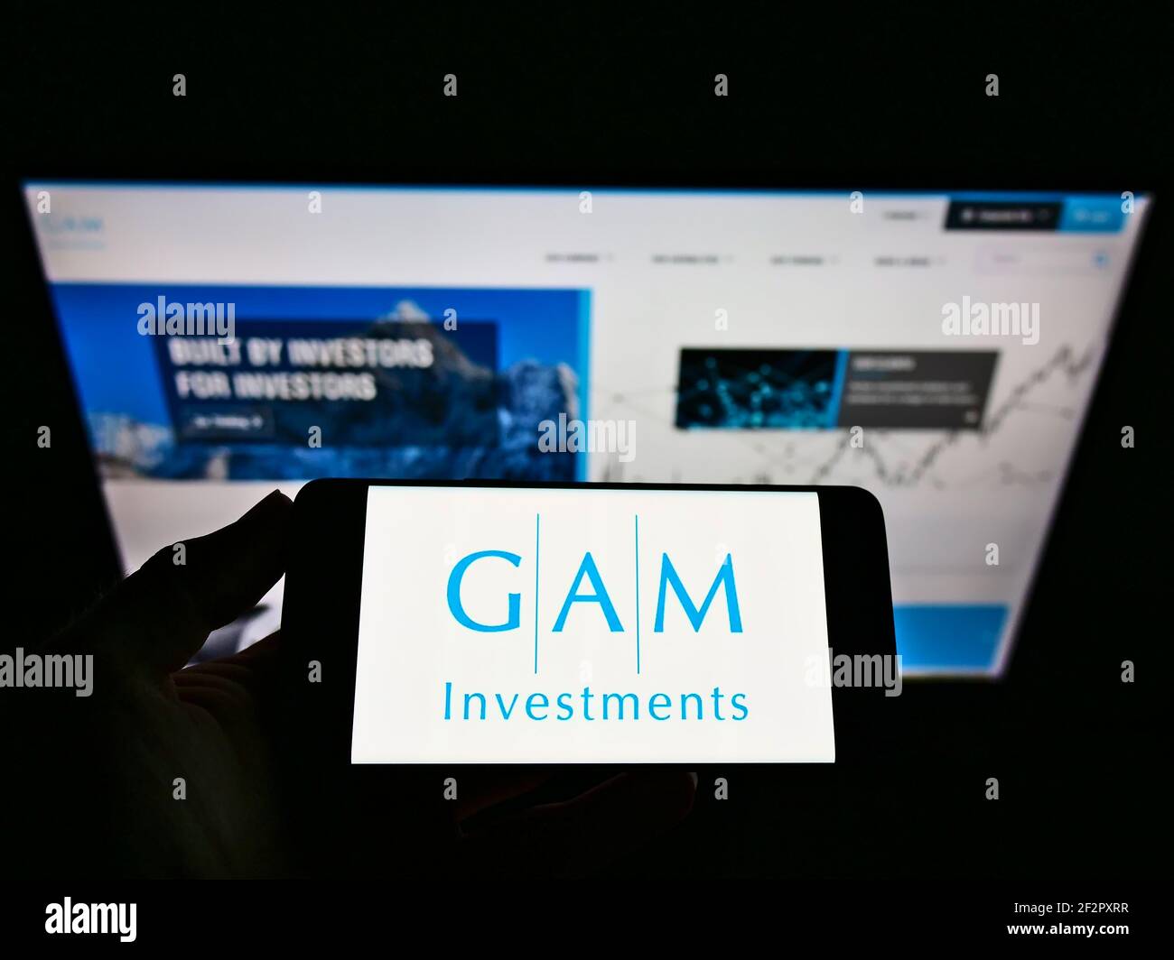 Person holding cellphone with business logo of Swiss financial services company GAM Investments on screen in front of webpage. Focus on phone display. Stock Photo