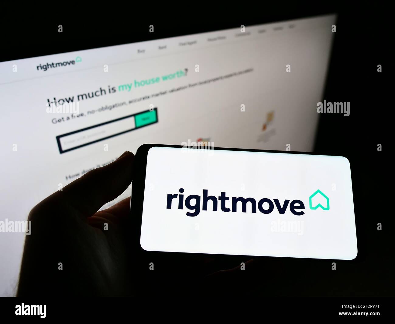 Person holding mobile phone with logo of British real estate online portal Rightmove plc on screen in front of web page. Focus on cellphone display. Stock Photo