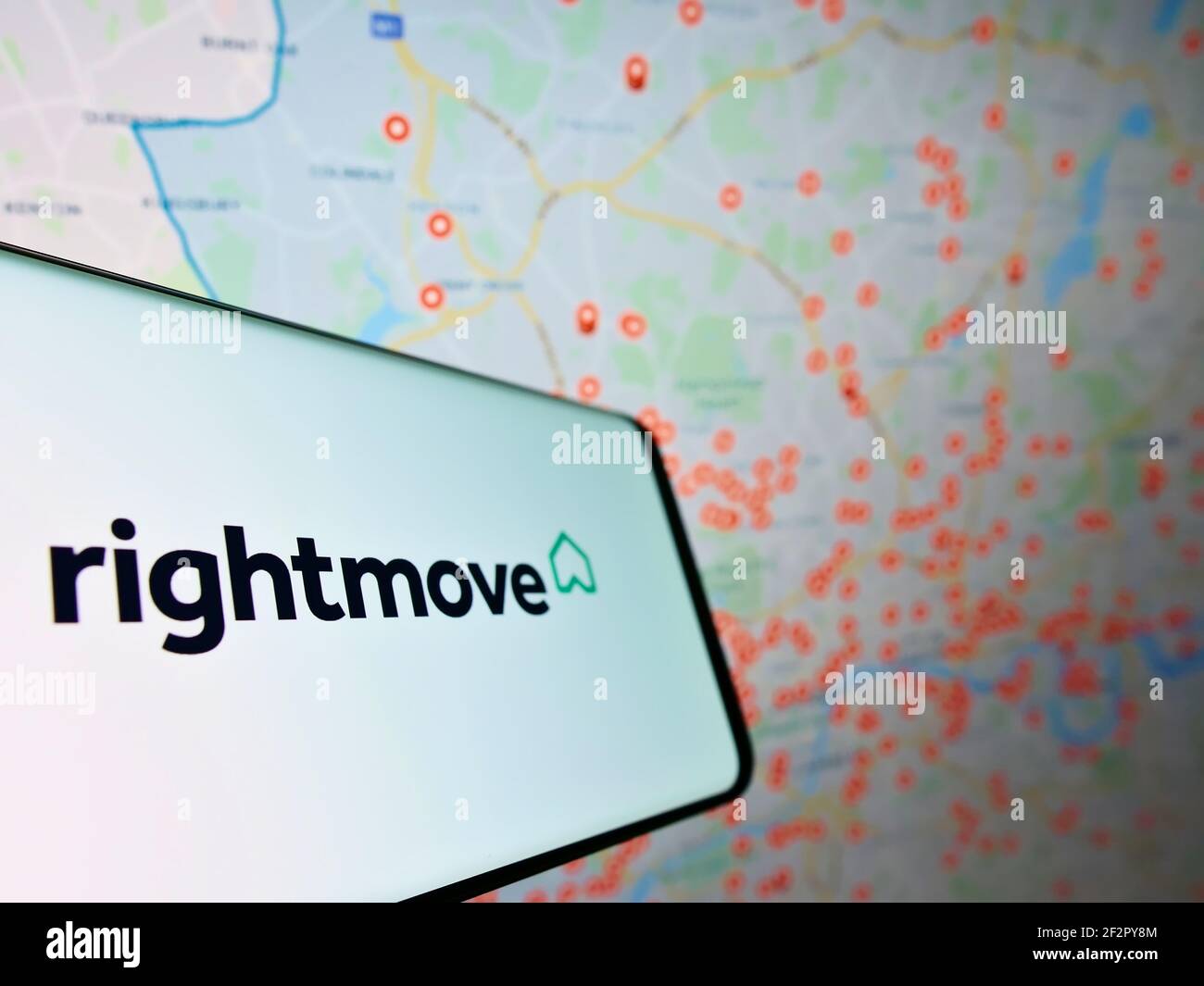Cellphone with logo of British real estate online portal Rightmove plc on screen in front of website with map. Focus on center of phone display. Stock Photo