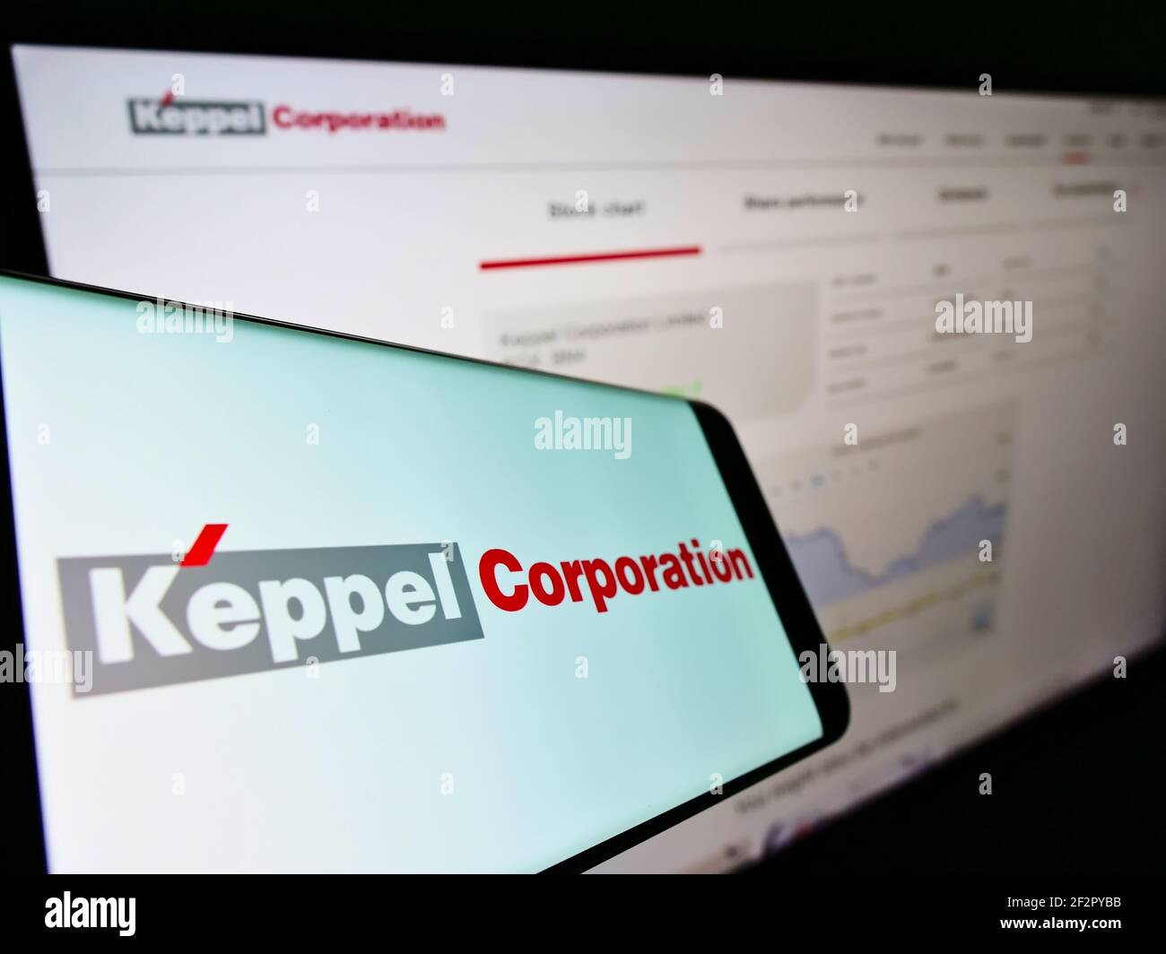 Mobile phone with business logo of Singaporean conglomerate Keppel Corporation on screen in front of webpage. Focus on center-right of phone display. Stock Photo