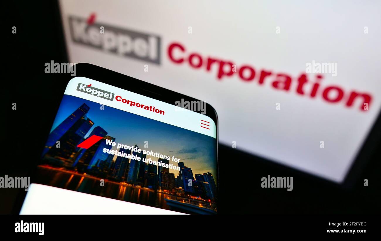 Mobile phone with company web page of Singaporean conglomerate Keppel Corporation on screen in front of logo. Focus on top-left of phone display. Stock Photo