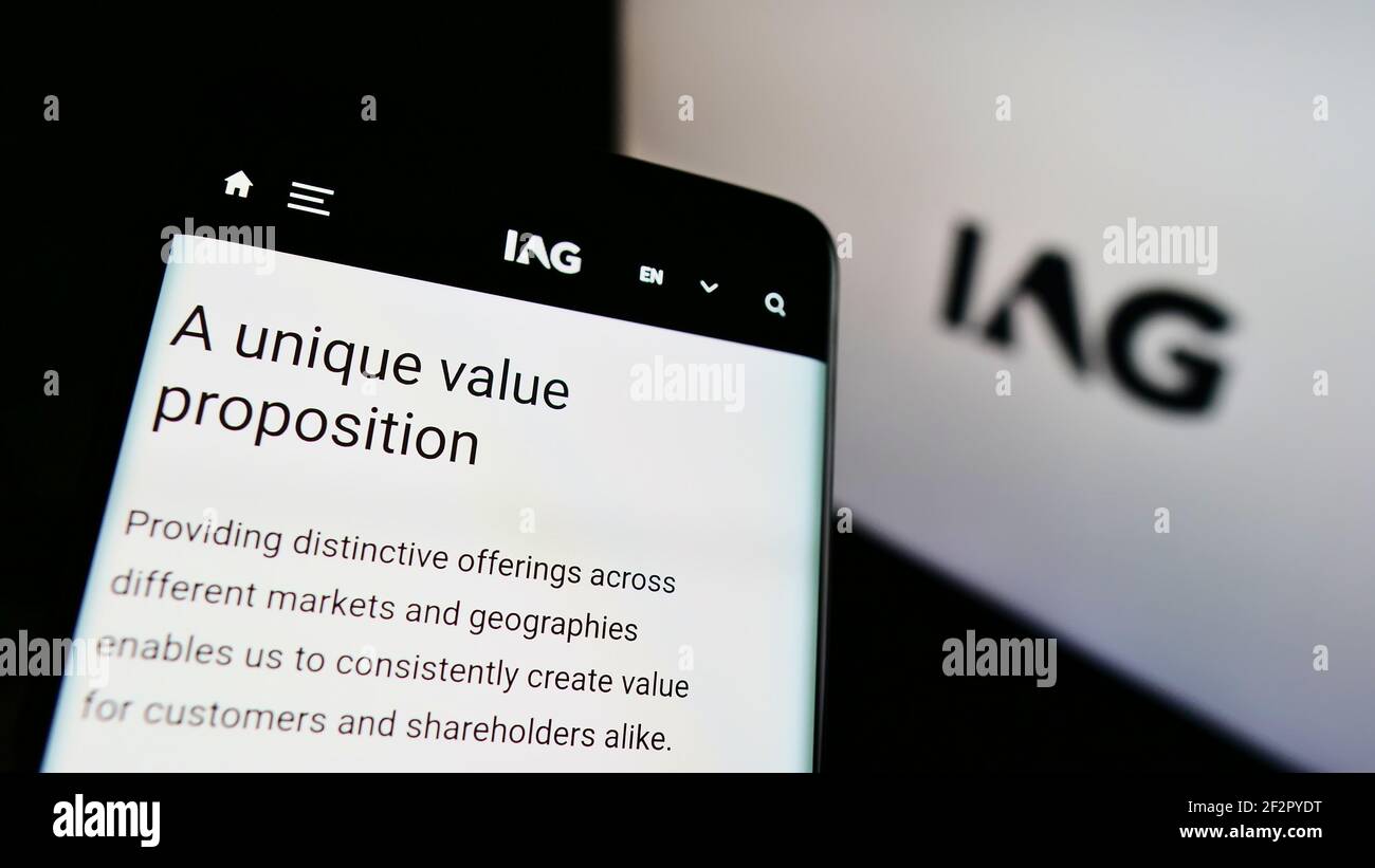 Smartphone with web page of airline company International Airlines Group (IAG) on screen in front of logo. Focus on top-left of phone display. Stock Photo