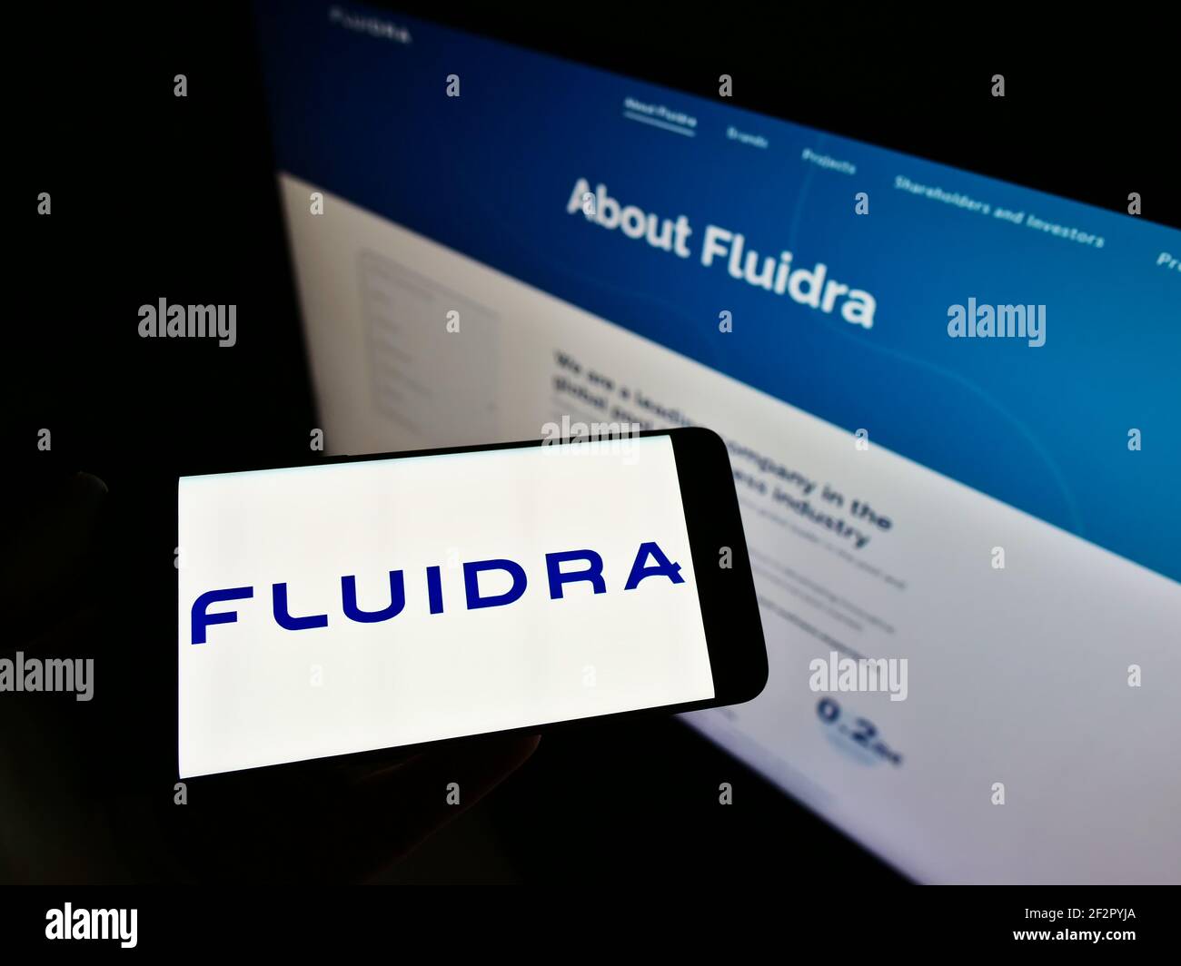 Person holding smartphone with logo of Spanish swimming pool company Fluidra S.A. on screen in front of website. Focus on phone display. Stock Photo