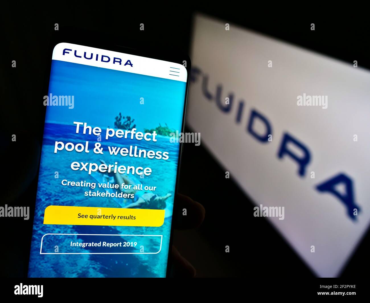 Person holding smartphone with web page of Spanish wellness company Fluidra S.A. on screen in front of logo. Focus on center of phone display. Stock Photo