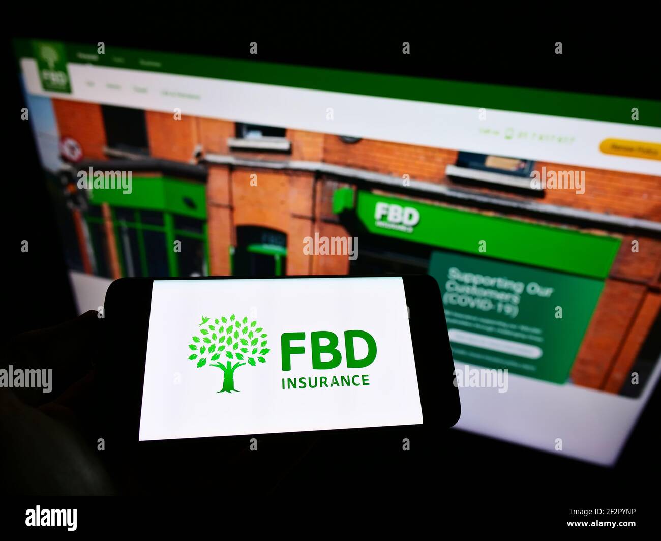 Person holding smartphone with logo of Irish insurance company FBD Holdings plc on screen in front of website. Focus on phone display. Stock Photo