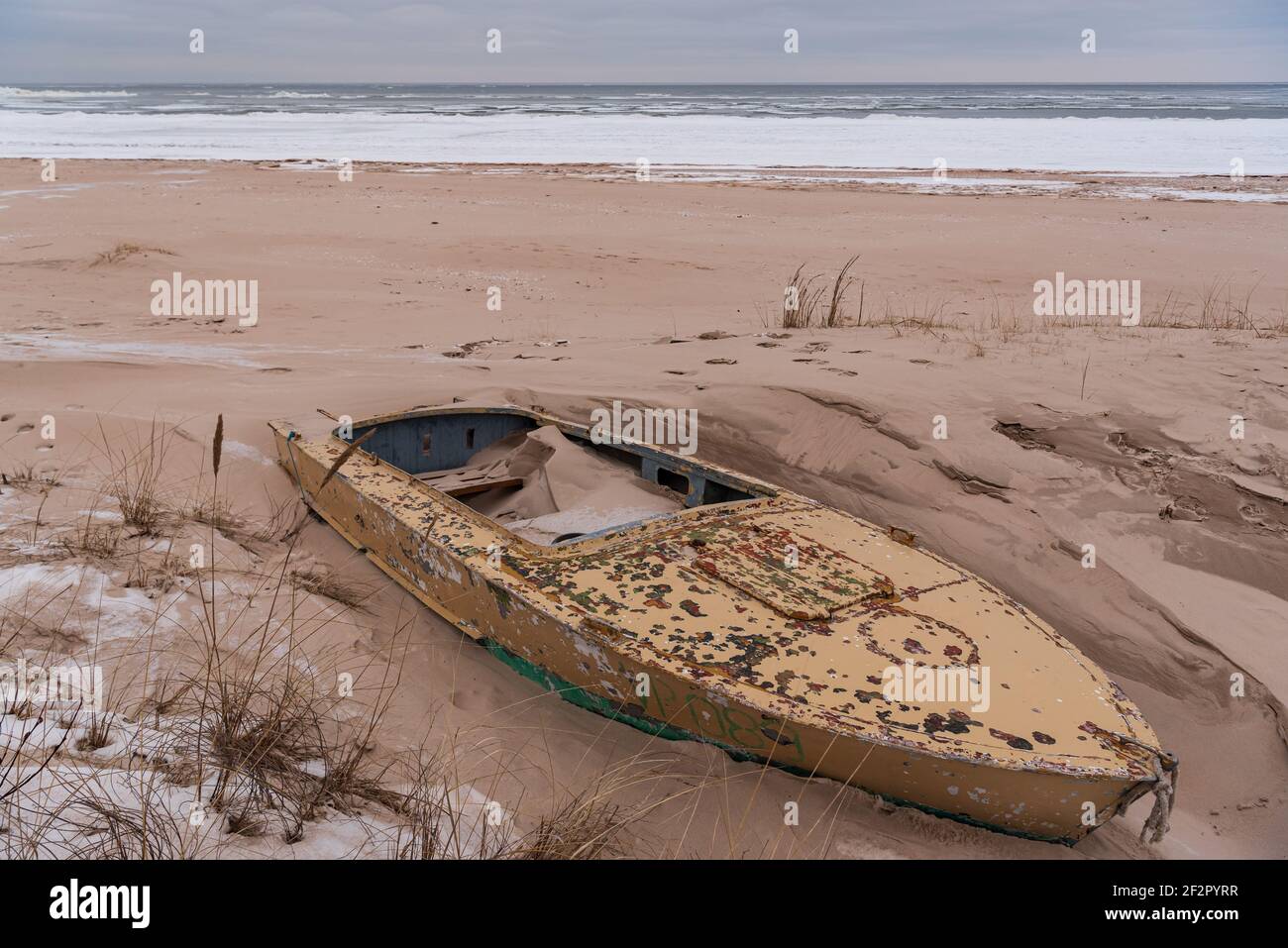 the boat is blown ashore in the sea sand close to the shoreline and the boat is made of yellow aluminum which has already peeled off in places Stock Photo