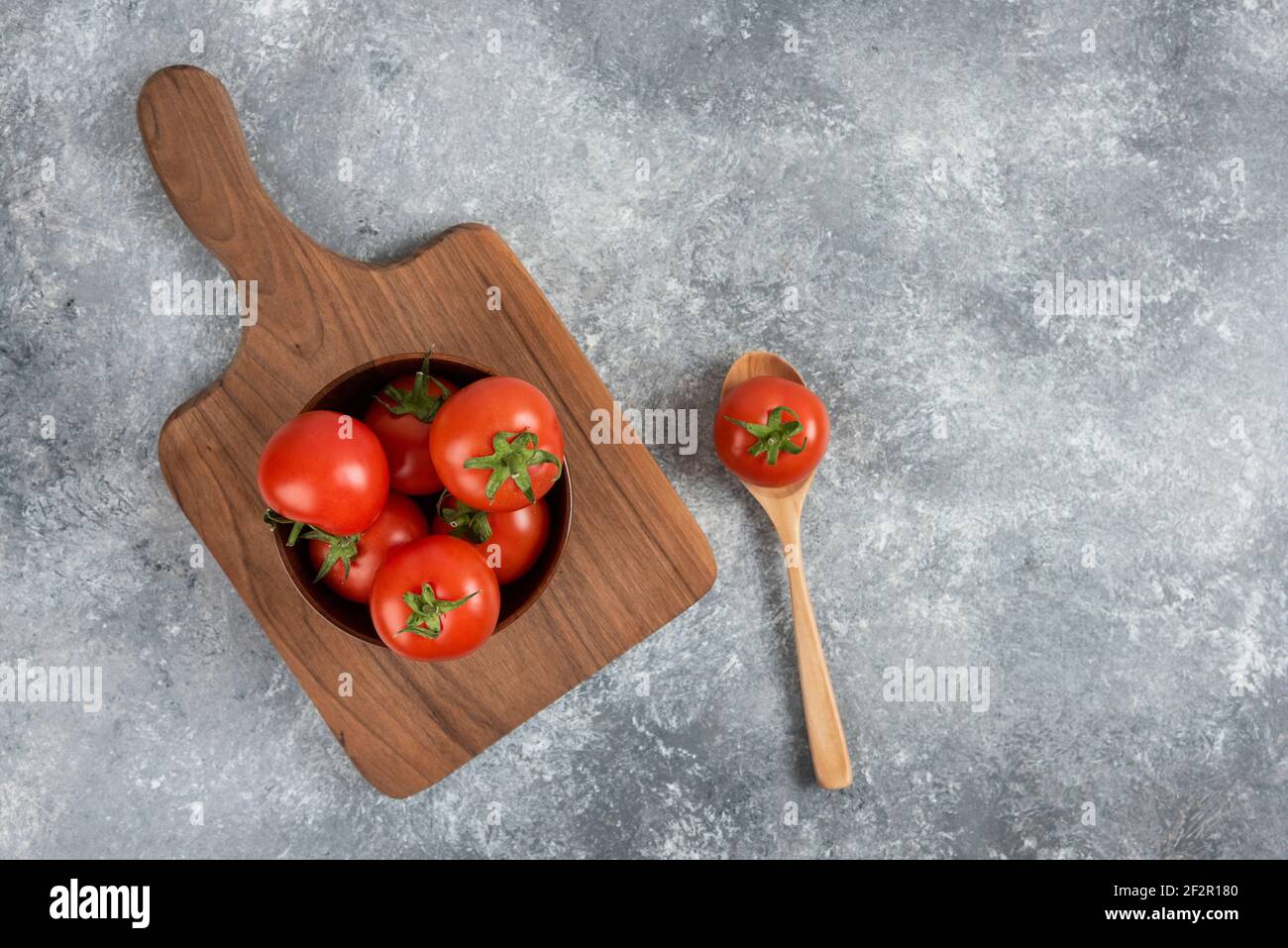 Wooden bowl of red fresh tomatoes on wooden cutting board Stock Photo