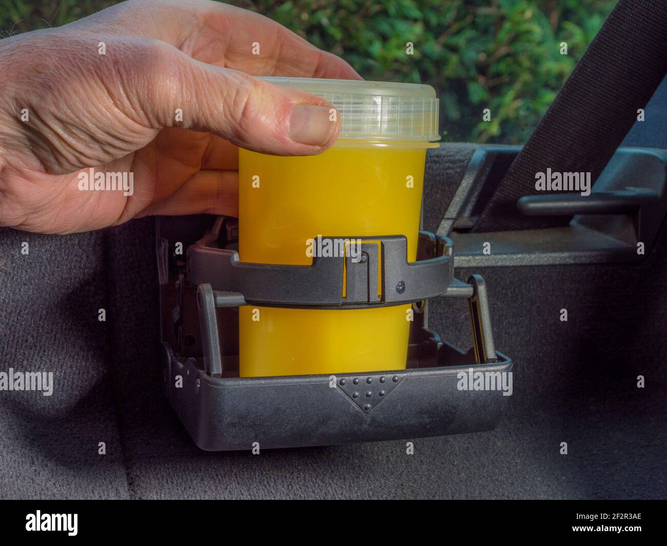 Closeup POV shot of a man’s hand holding a plastic container with a cold orange juice drink inside, standing in a foldaway cupholder in a vehicle. Stock Photo
