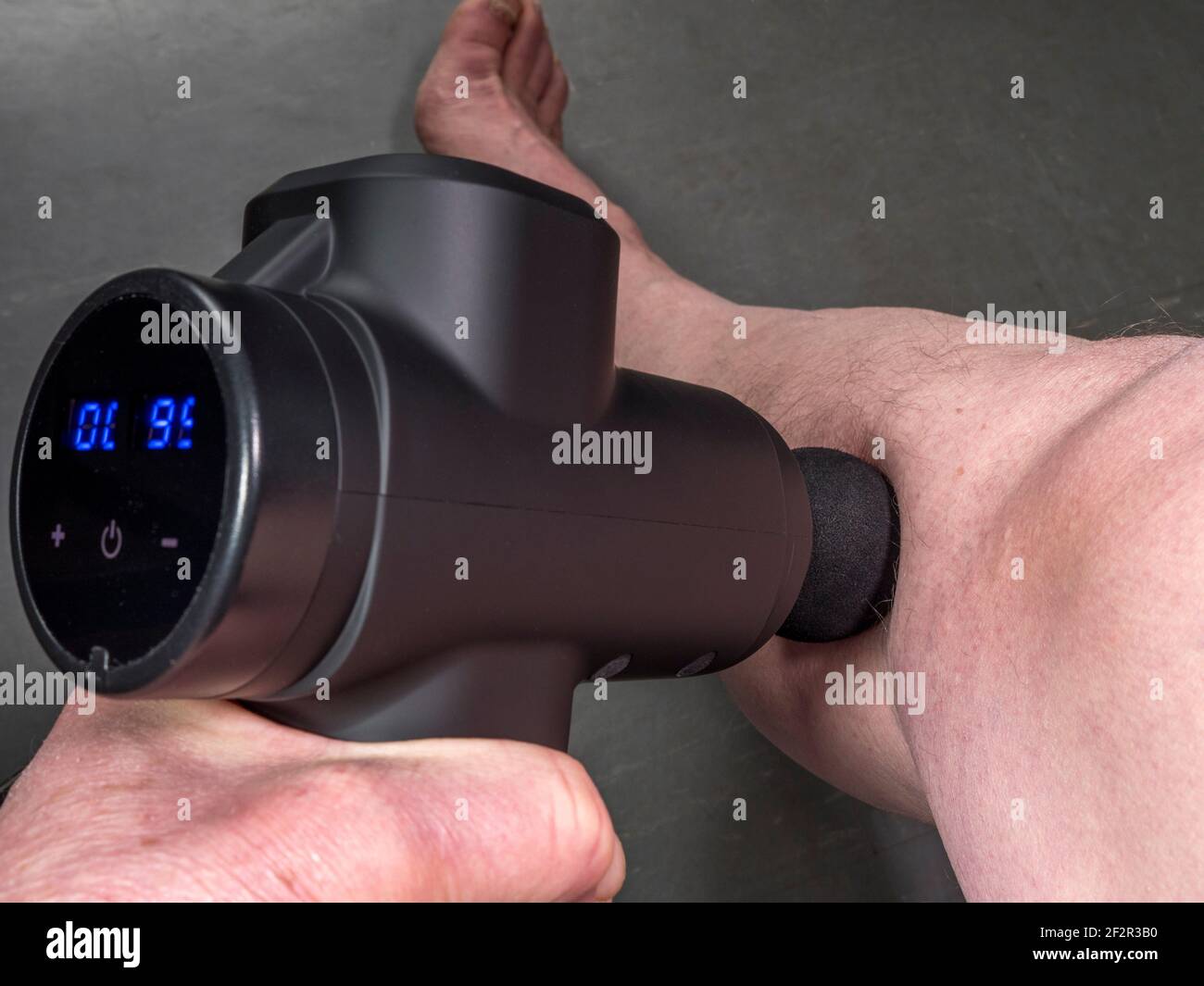 Closeup POV shot of a modern battery operated massage gun being used on a man’s tight calf muscle. Stock Photo