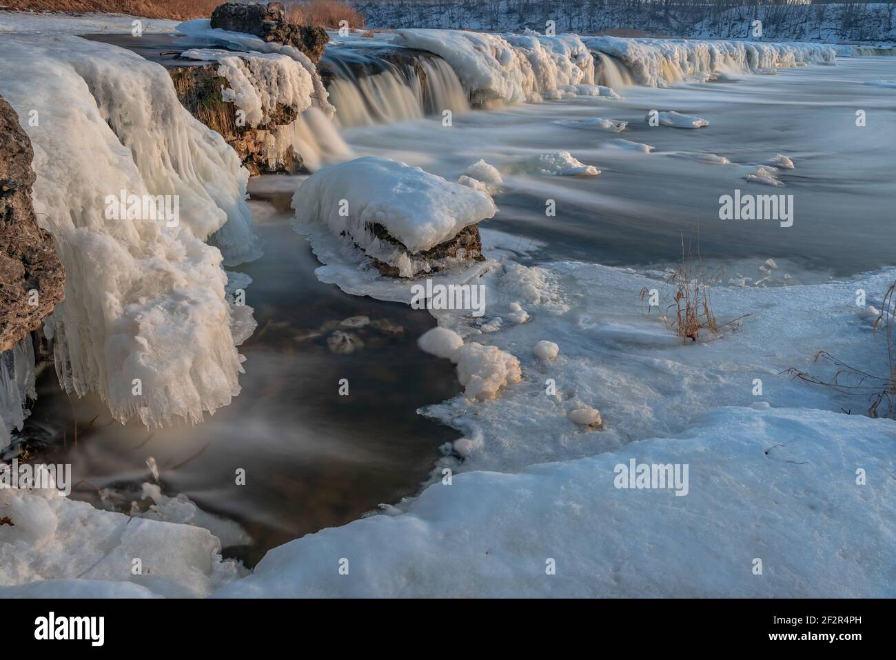 a wide waterfall in the winter with ice and snow merged in a long ...