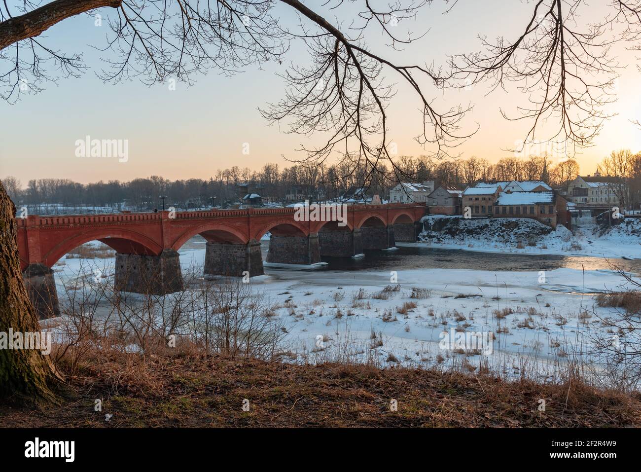 an ancient stone and red brick bridge over the river which in places is still frozen by a layer of ice Stock Photo