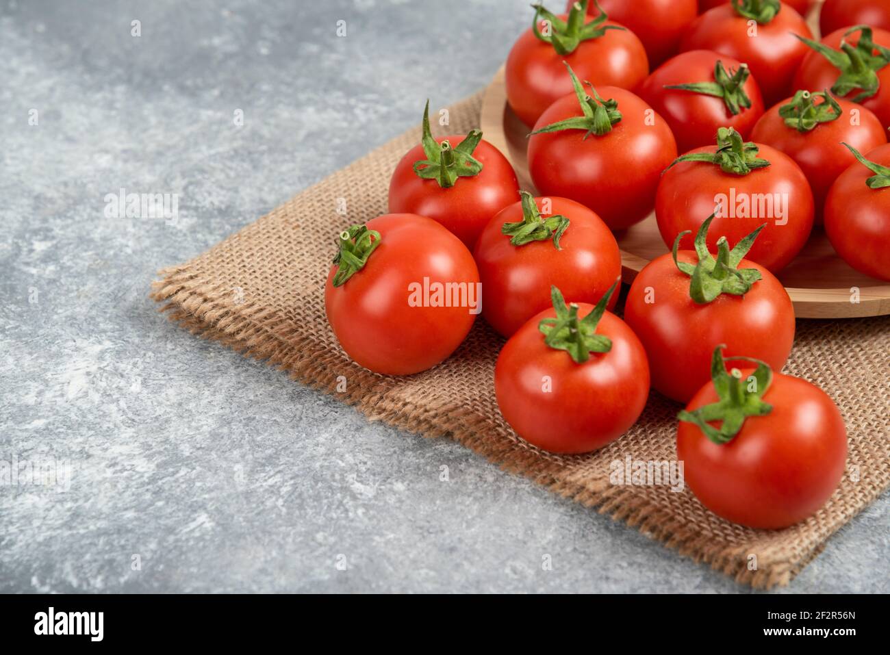 Bunch of red fresh tomatoes with sack cloth on marble surface Stock Photo