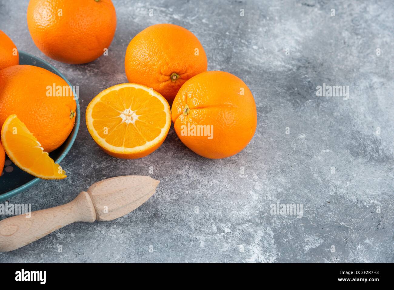 A bowl full of sliced and whole juicy orange fruits with wooden reamer Stock Photo