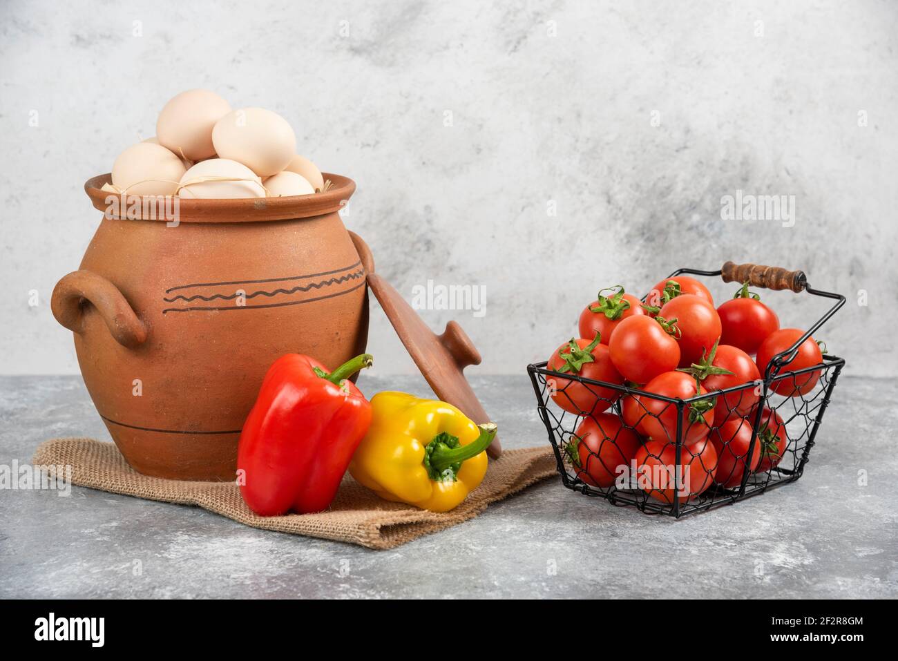 Pot of raw eggs, tomatoes and bell peppers on marble background Stock Photo