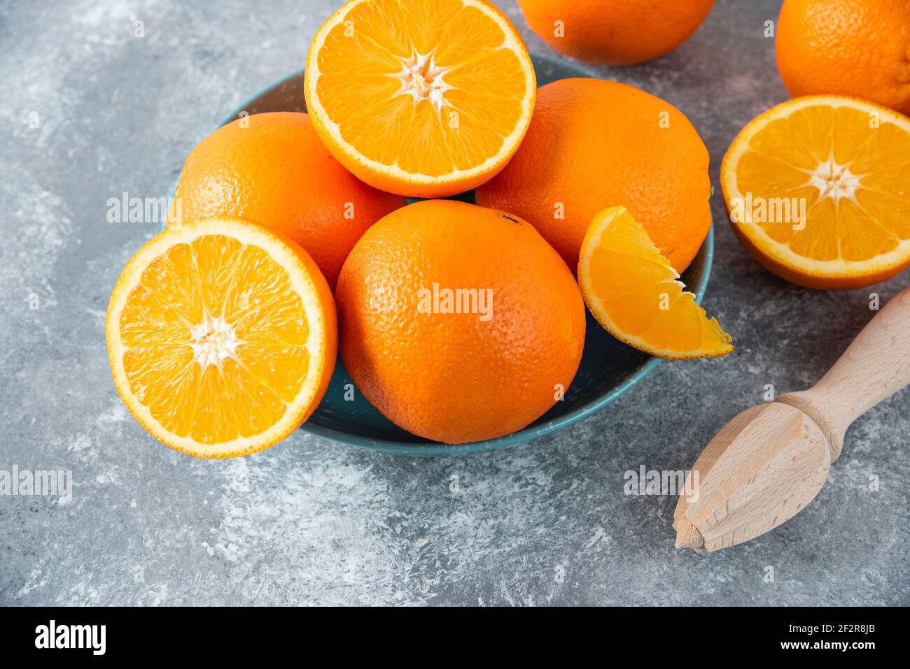 A bowl full of sliced and whole juicy orange fruits with wooden reamer Stock Photo