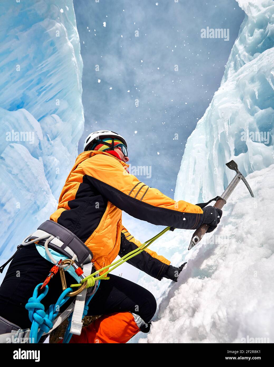 Woman is climbing frozen waterfall with ice axe in orange jacket in the mountains Stock Photo