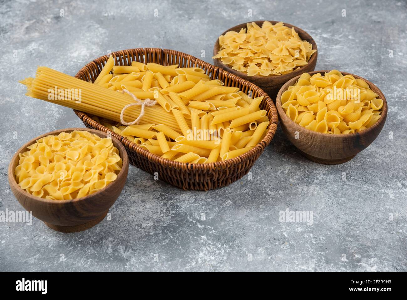Pile of various uncooked dry pasta in wicker basket and wooden bowls Stock Photo