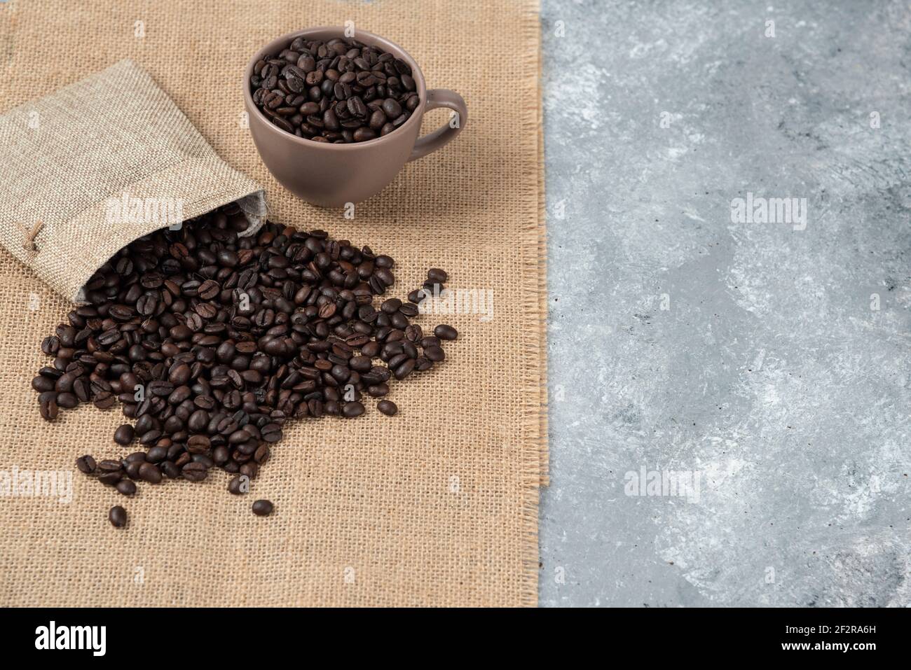 Bunch of medium roasted coffee beans out of sackcloth on marble surface Stock Photo