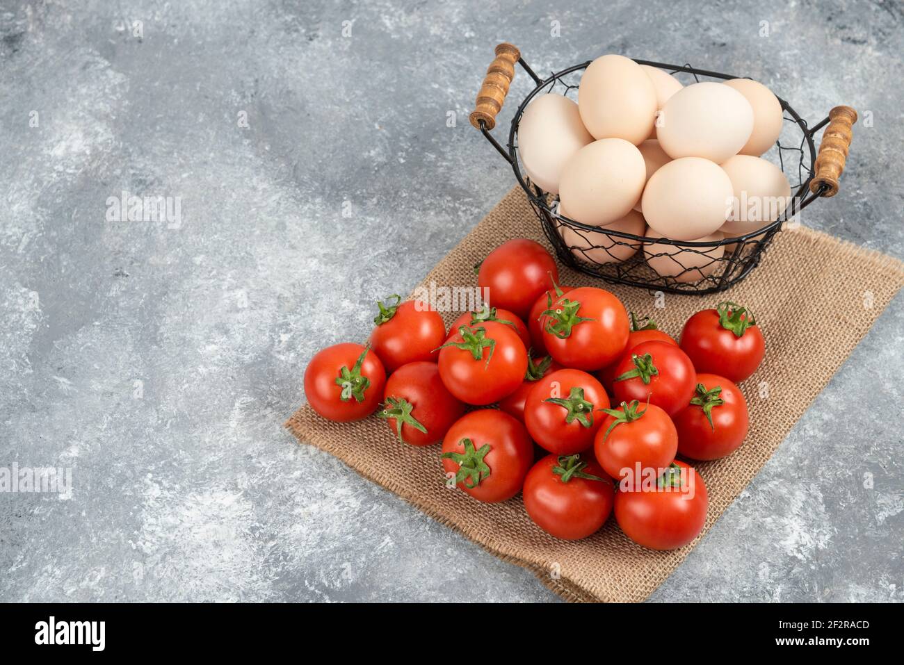 Basket of fresh uncooked eggs and ripe tomatoes on marble background Stock Photo