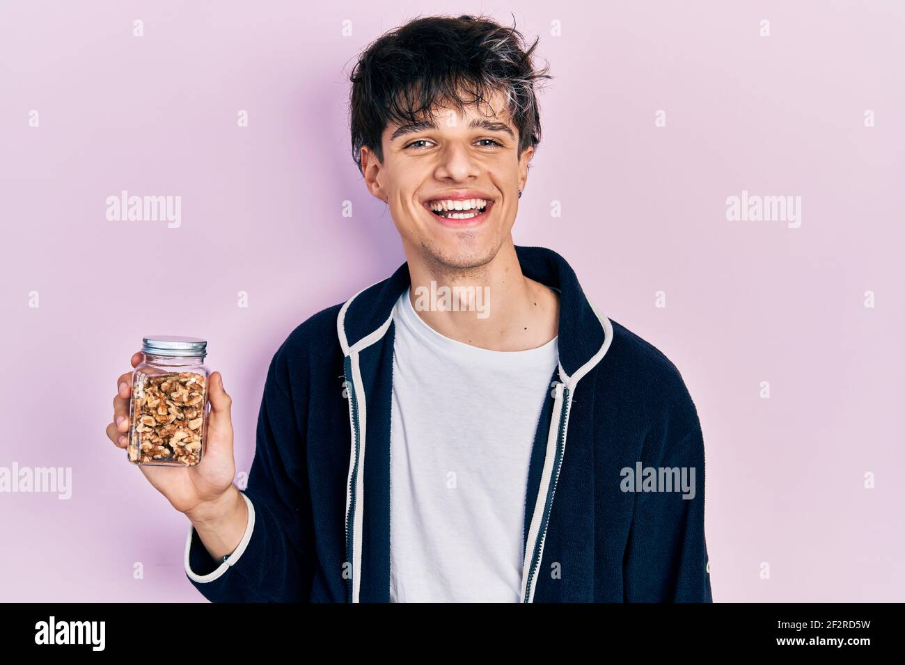 Handsome hipster young man holding walnuts looking positive and happy standing and smiling with a confident smile showing teeth Stock Photo