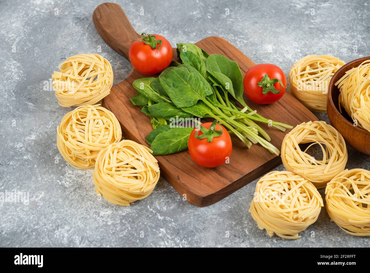 Wooden board with fresh vegetables and raw noodles on marble surface Stock Photo