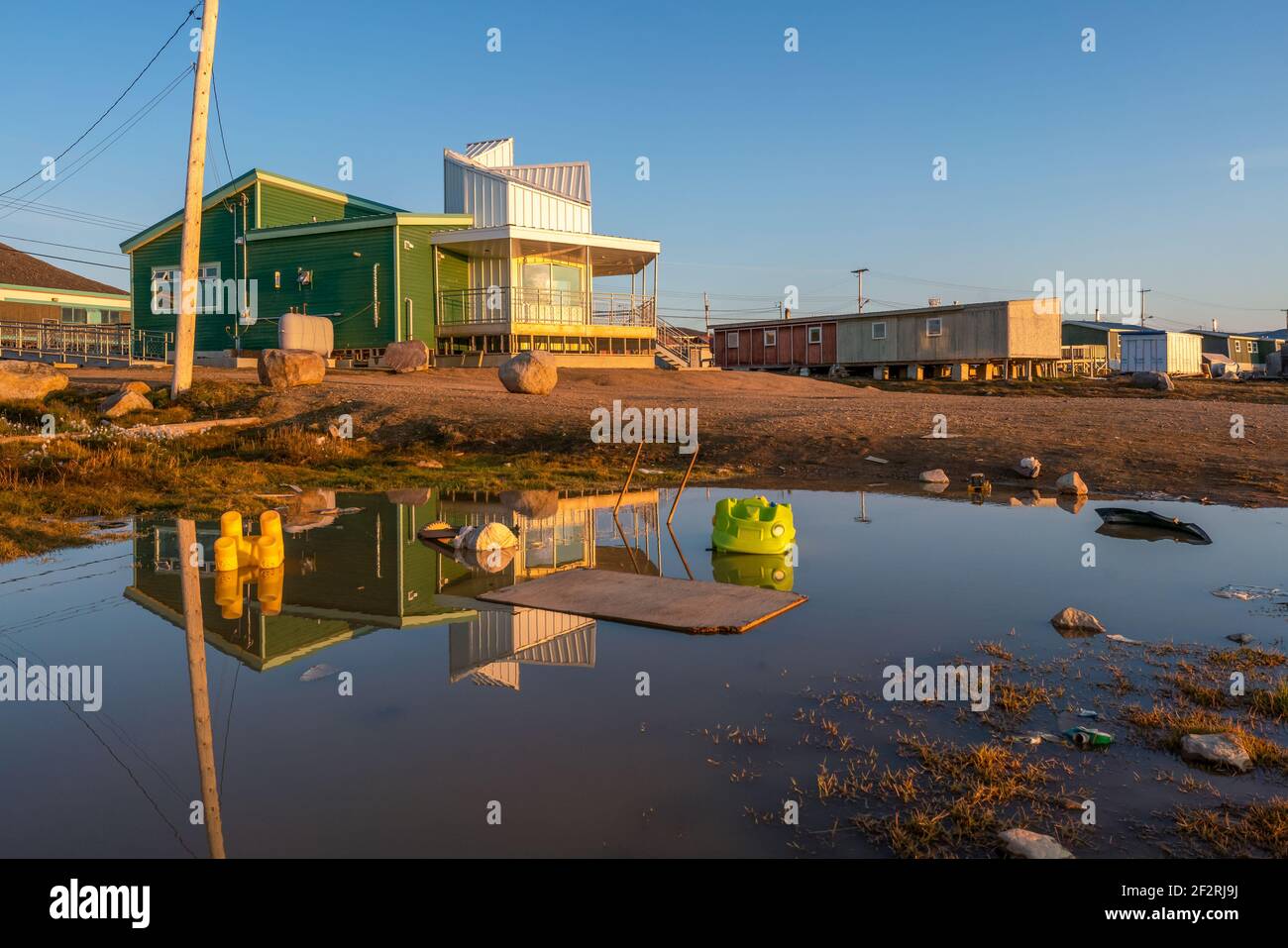 Golden hour in Inuit community of Qikiqtarjuaq, Broughton Island, Nunavut, Canada. Parks Canada building reflection on water surface. Settlement in Stock Photo