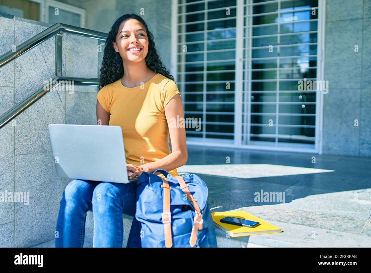 Young african american student girl using laptop sitting on stairs at ...