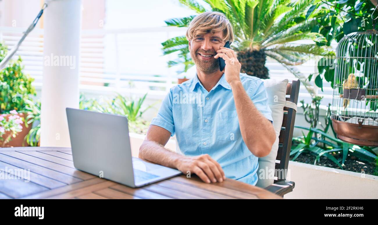 Middle age handsome man working at home using computer laptop and speaking on smartphone Stock Photo