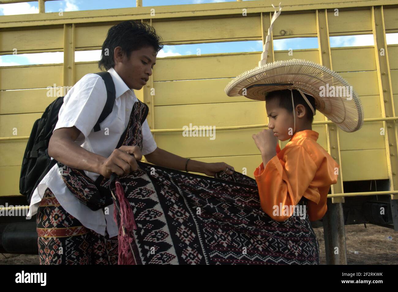 A young man and a child getting ready with traditional attire during a preparation for ceremonial event to release the island's endemic snake-necked turtle species (Chelodina mccordi) bred in captivity back to its home island. Rote Island, East Nusa Tenggara, Indonesia. Stock Photo