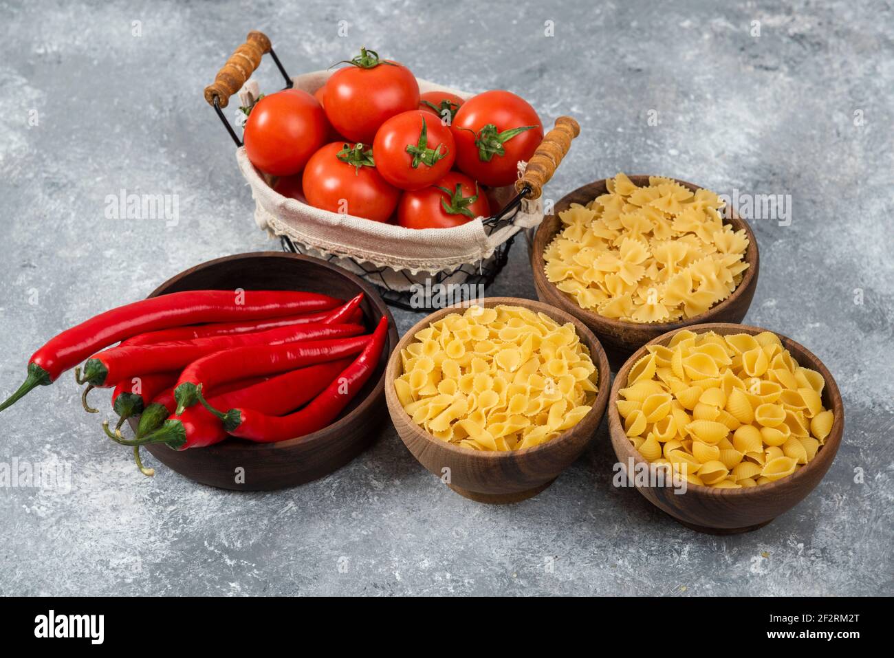 Wooden bowls of raw pasta with red chili peppers and tomatoes Stock Photo