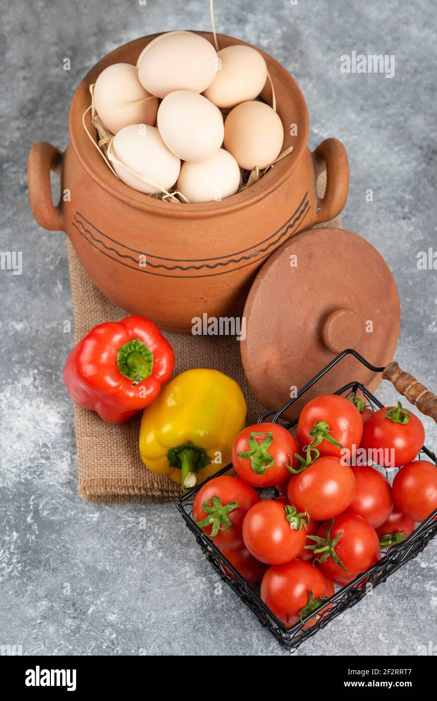 Pot of raw eggs, tomatoes and bell peppers on marble background Stock Photo