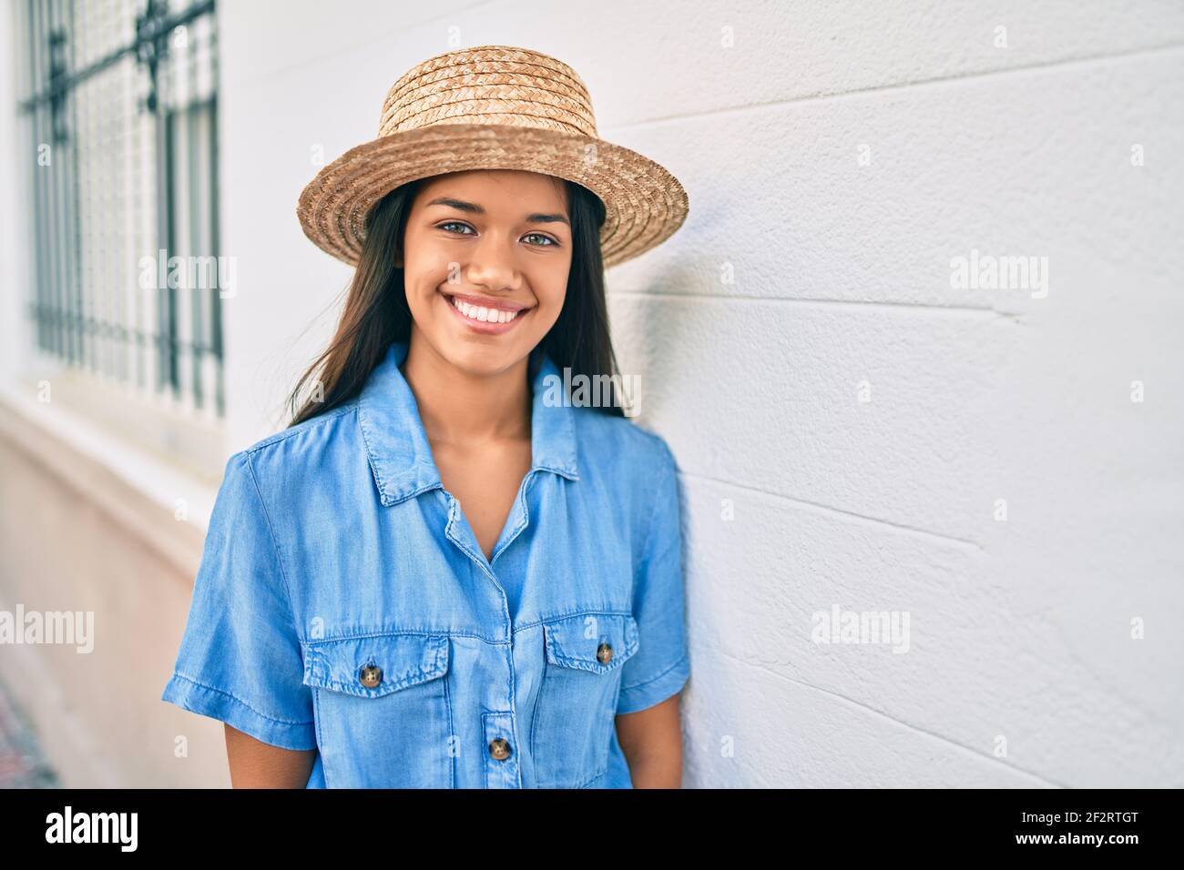 Young latin tourist girl on vacation smiling happy leaning on the wall ...