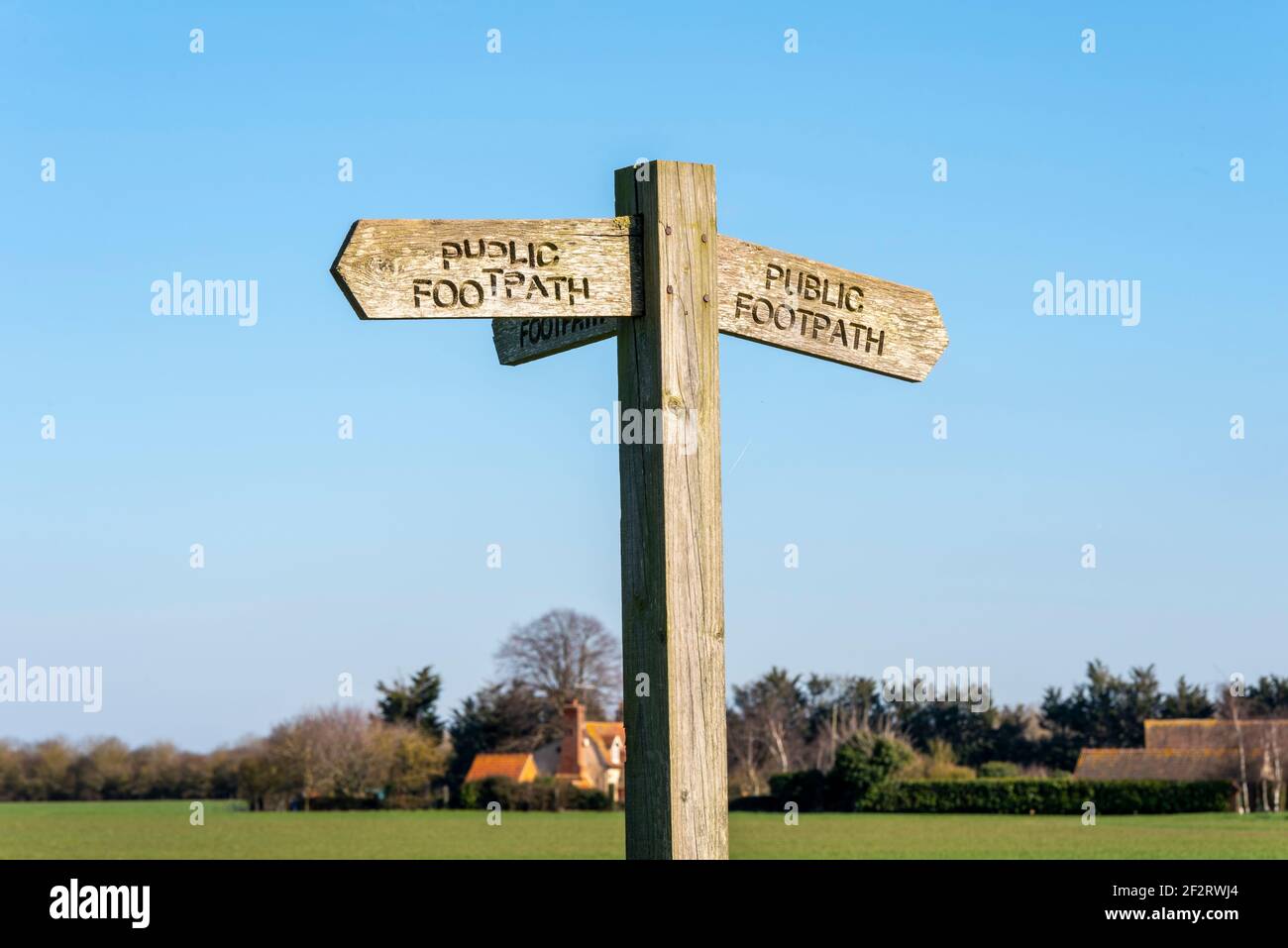 Old wooden public footpath sign in a rural area near Stambridge in the Essex countryside. Isolated against blue sky. Text not straight Stock Photo