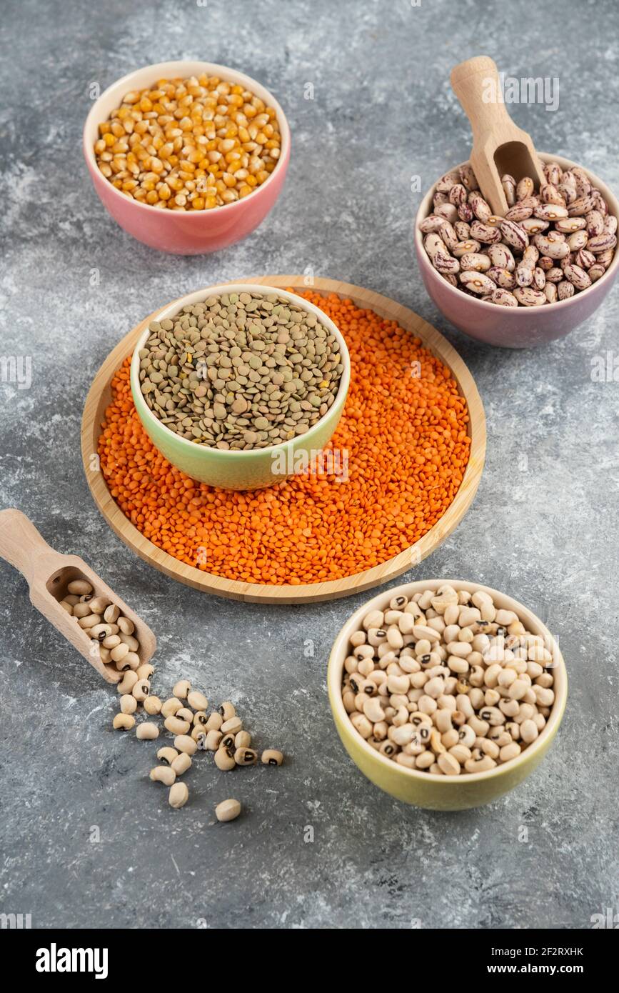 Colorful bowls of various uncooked beans, lentils and corns on marble surface Stock Photo