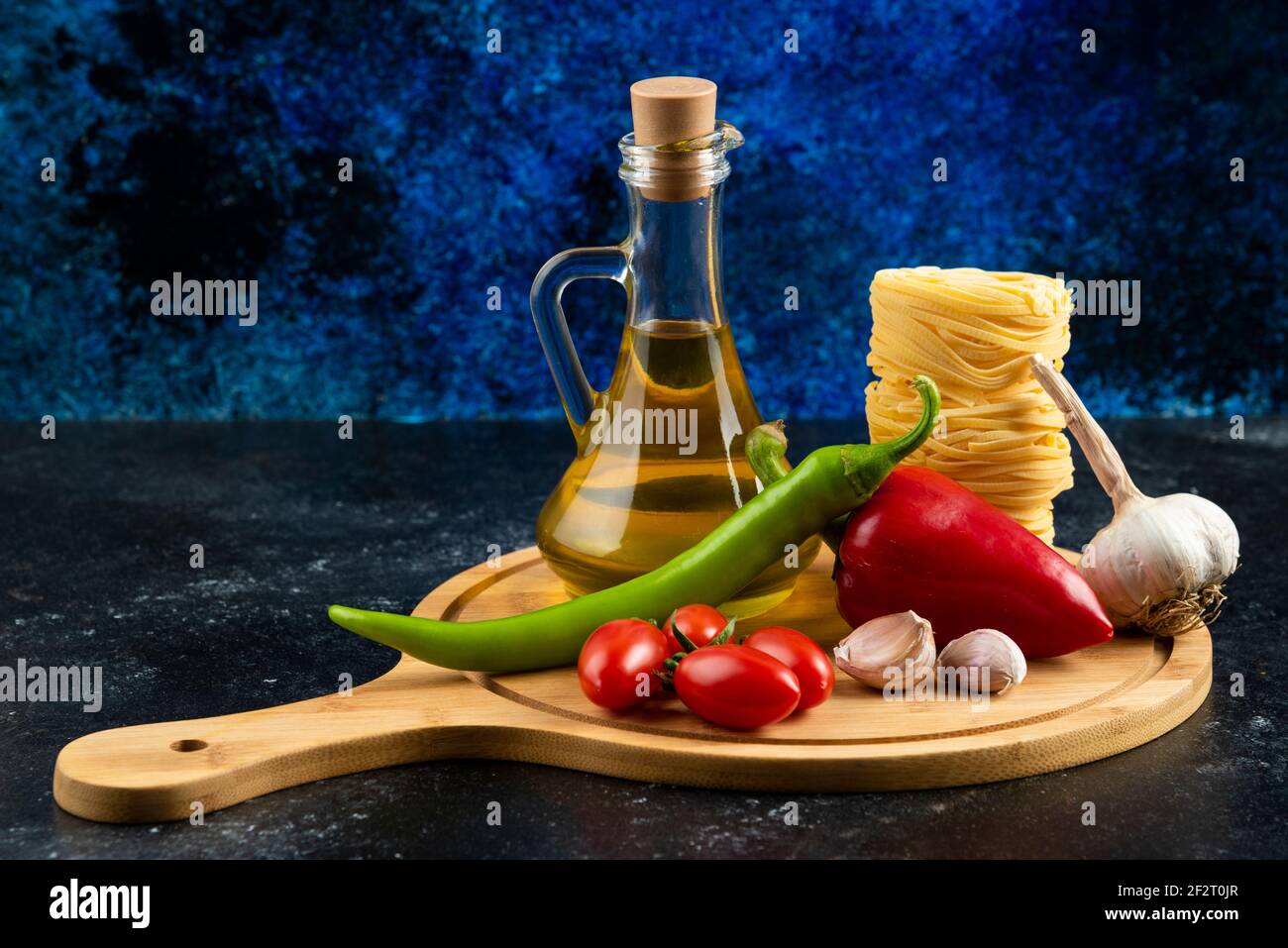 Various pasta, oil and vegetables on wooden board Stock Photo