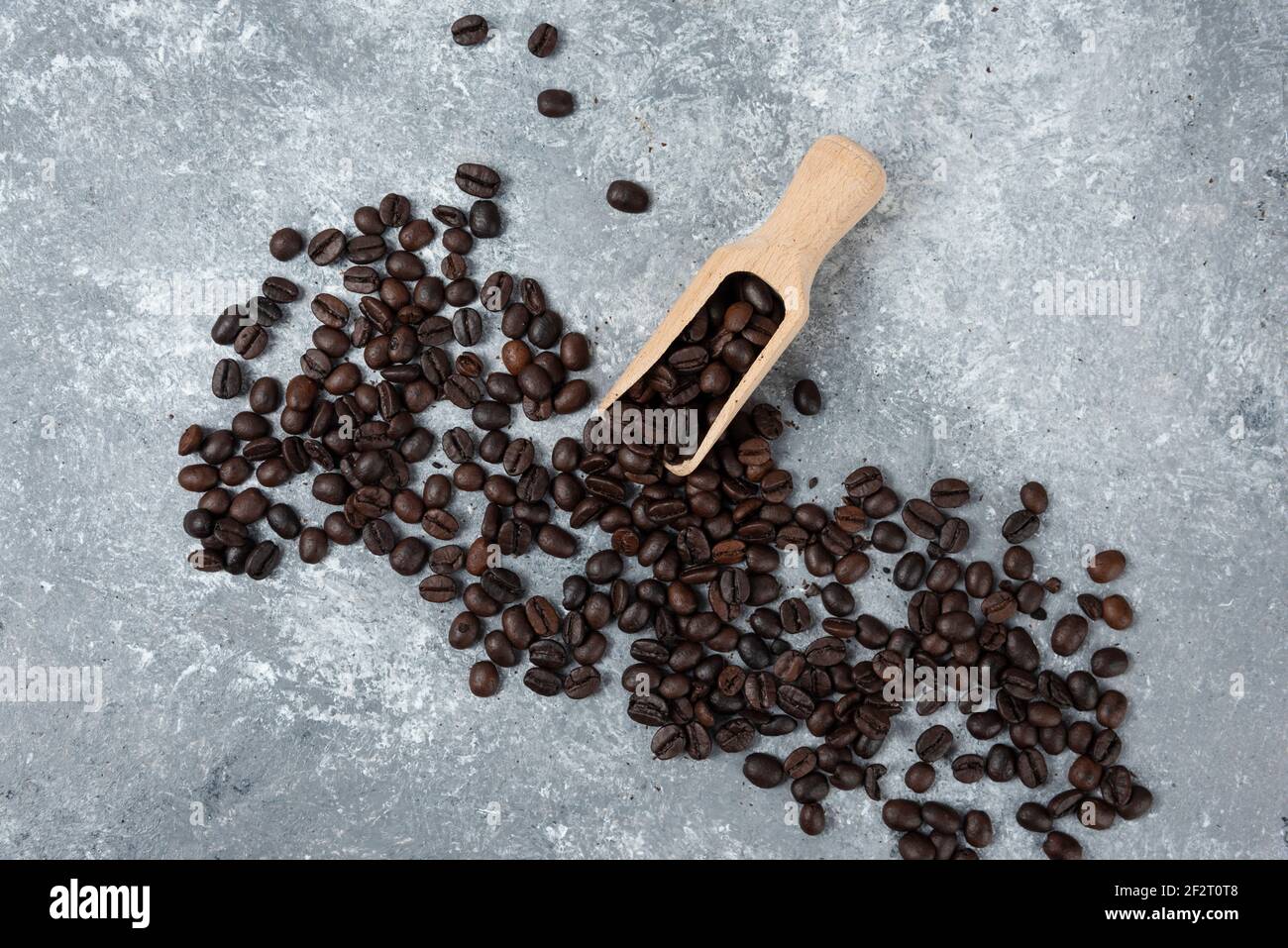 Wooden spoon and scattered roasted coffee beans on marble surface Stock Photo
