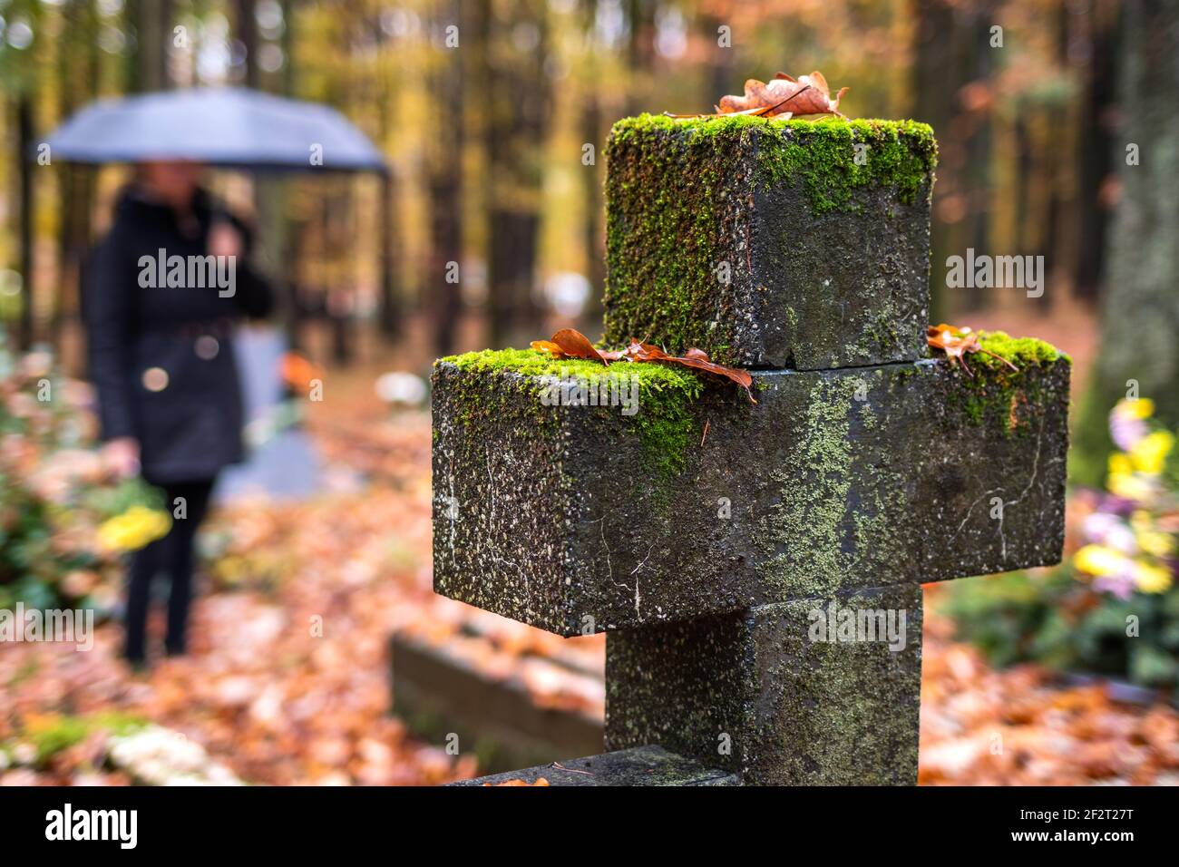 Religious cross in cemetery.  Mourning woman in black standing next to tombstone in rain.  Silent memory for dead relatives Stock Photo